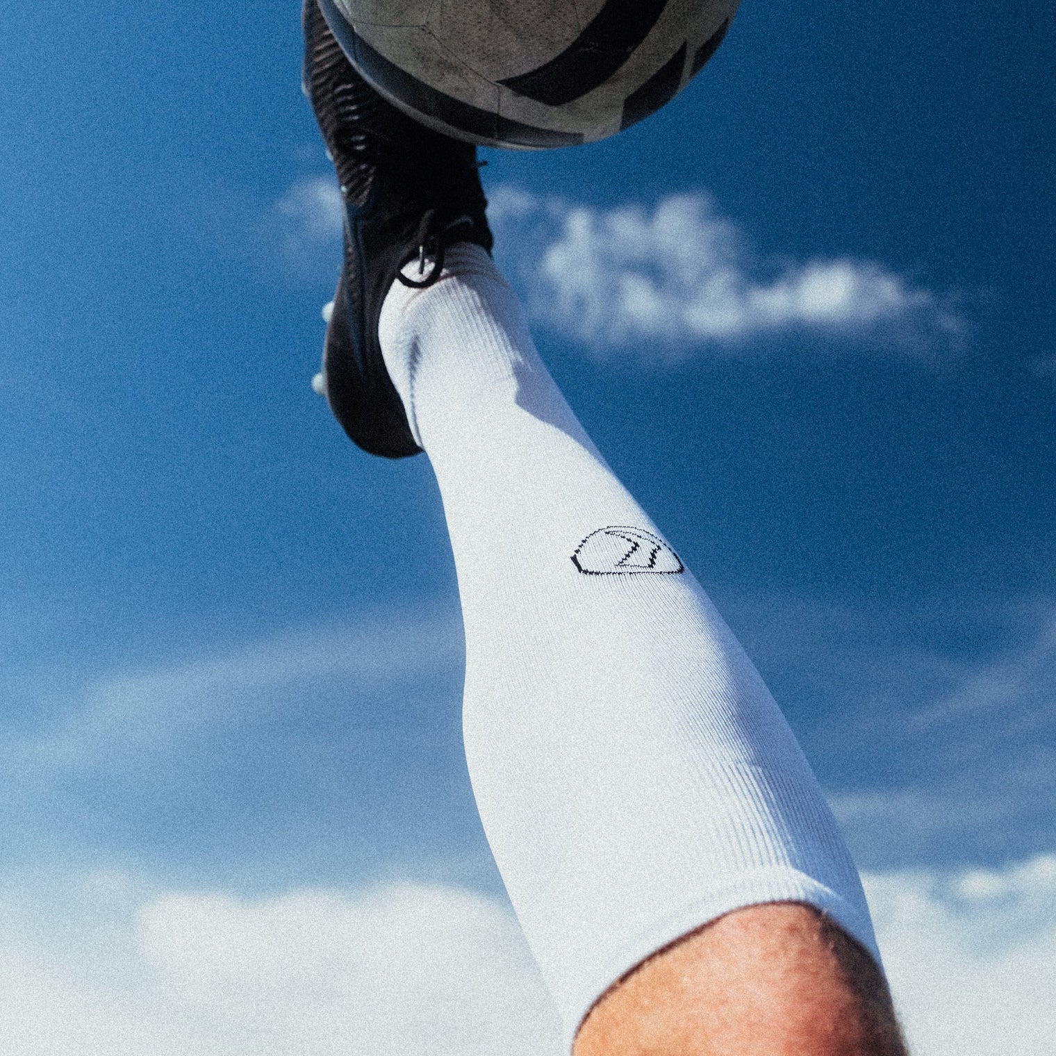 Person kicking a soccer ball against a blue sky